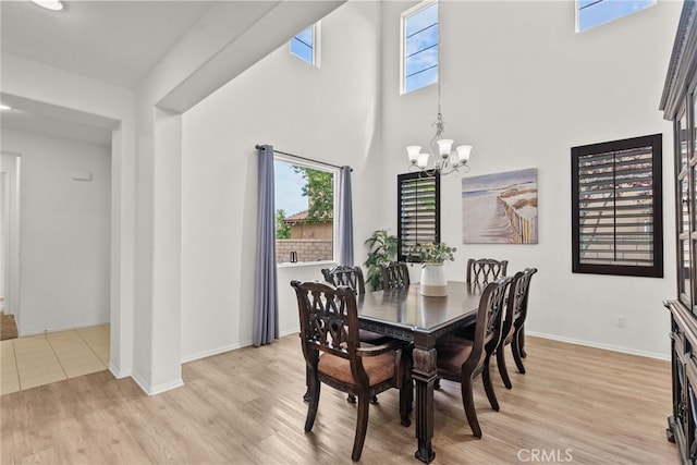 dining room with an inviting chandelier, light wood-type flooring, baseboards, and a high ceiling