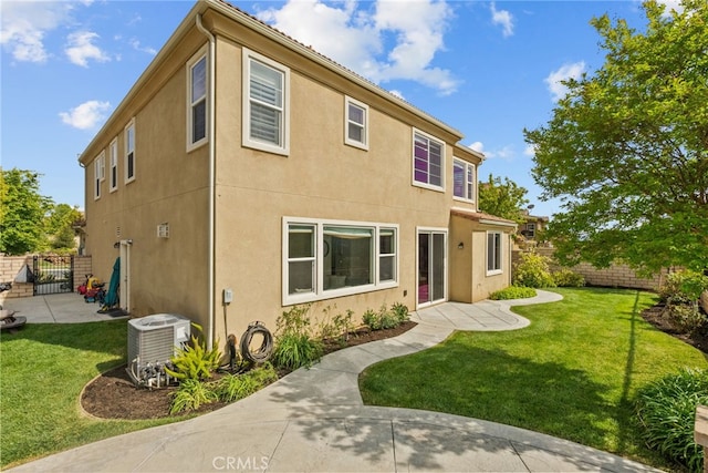 rear view of house with central AC unit, a yard, a gate, stucco siding, and fence