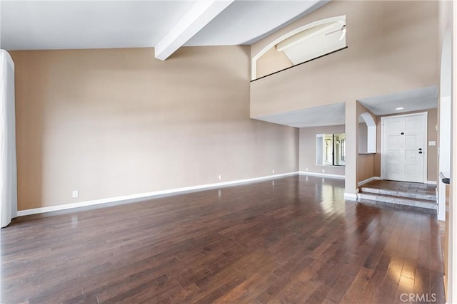 unfurnished living room featuring baseboards, wood finished floors, beam ceiling, arched walkways, and a high ceiling