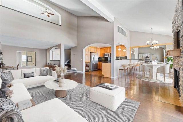 living room featuring a fireplace, high vaulted ceiling, dark wood-style floors, a chandelier, and arched walkways