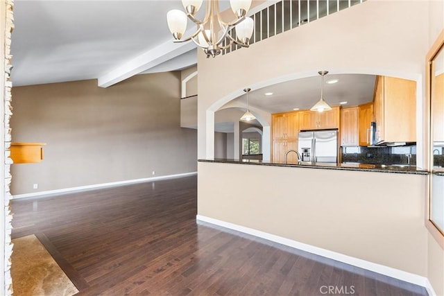 kitchen with stainless steel fridge, dark countertops, arched walkways, baseboards, and dark wood finished floors