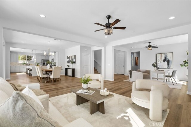 living room with stairway, ceiling fan with notable chandelier, light wood finished floors, and recessed lighting