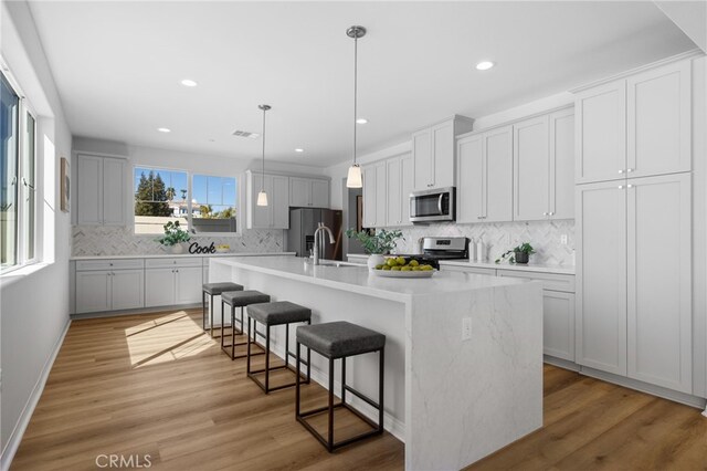 kitchen with an island with sink, stainless steel appliances, backsplash, light countertops, and a kitchen bar