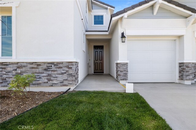 doorway to property featuring stucco siding, an attached garage, driveway, and stone siding