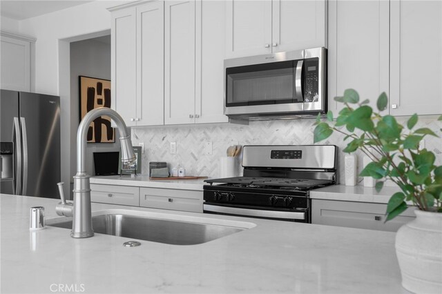 kitchen featuring backsplash, appliances with stainless steel finishes, a sink, and white cabinetry