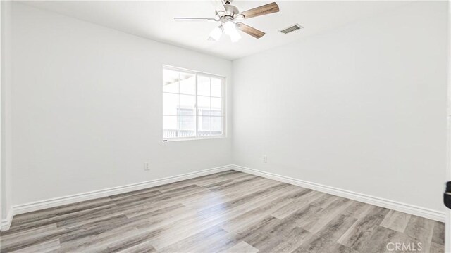 empty room featuring wood finished floors, visible vents, baseboards, and ceiling fan
