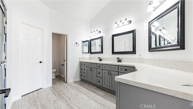 full bathroom featuring baseboards, wood finished floors, toilet, and vanity