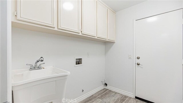 clothes washing area featuring a sink, light wood-type flooring, cabinet space, baseboards, and washer hookup