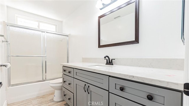 full bathroom featuring wood finished floors, visible vents, toilet, vanity, and bath / shower combo with glass door