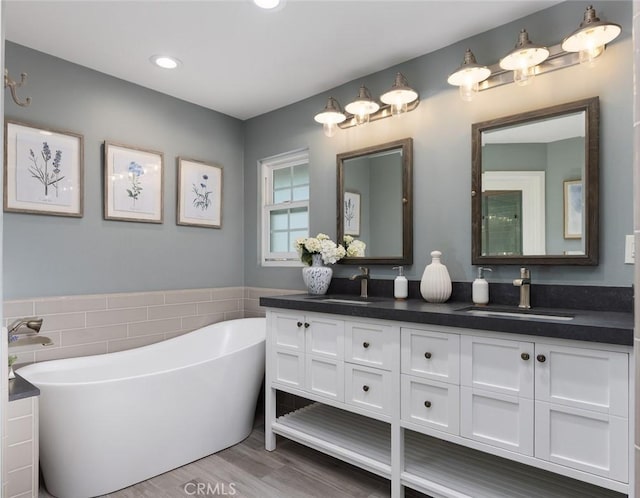 full bath featuring tile walls, a soaking tub, a sink, and double vanity