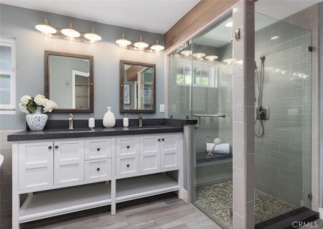 full bath featuring a stall shower, wood finished floors, double vanity, and a sink
