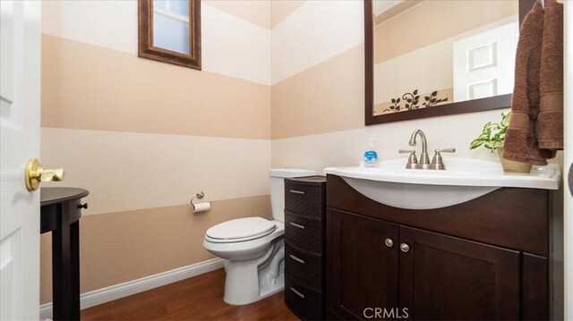 half bathroom with baseboards, wood finished floors, vanity, and toilet