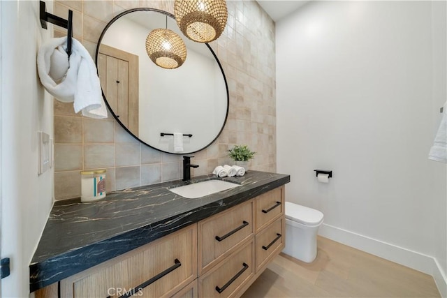 bathroom with wood finished floors, toilet, vanity, baseboards, and decorative backsplash