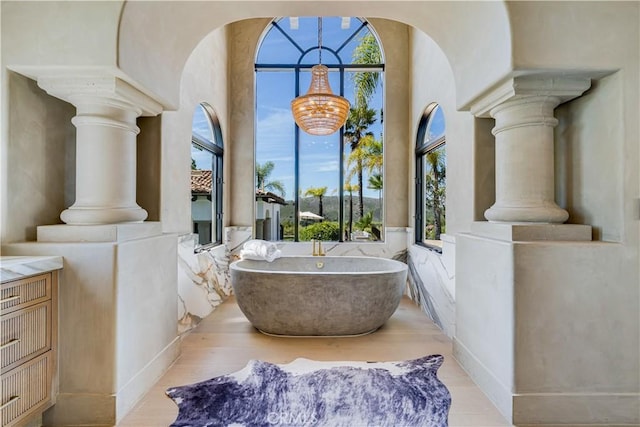 bathroom featuring a soaking tub, wood finished floors, and decorative columns