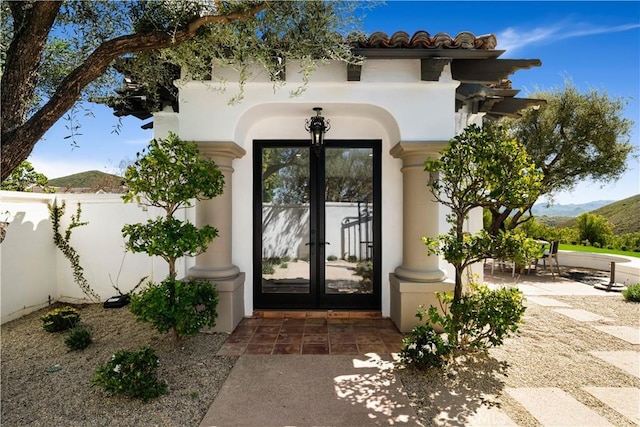 doorway to property with french doors, a mountain view, stucco siding, and fence