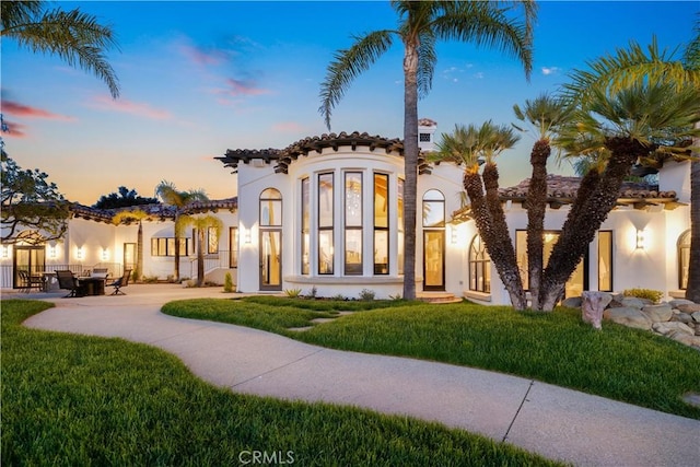 view of front of property featuring curved driveway, stucco siding, a patio area, a tile roof, and a lawn