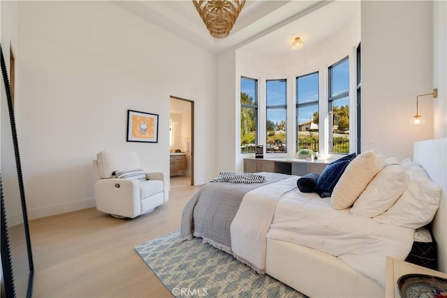 bedroom with light wood-style floors, ensuite bath, baseboards, and a high ceiling