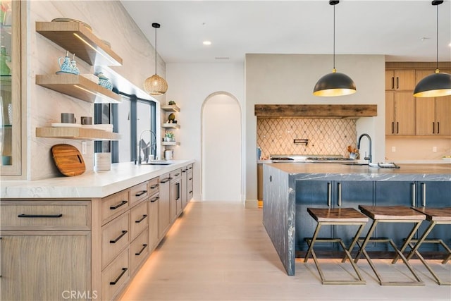 kitchen featuring light brown cabinets, a kitchen breakfast bar, open shelves, a sink, and backsplash