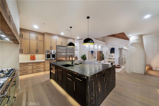 kitchen featuring a sink, arched walkways, light wood-style floors, pendant lighting, and built in fridge