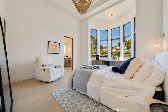 bedroom featuring connected bathroom, baseboards, a towering ceiling, and light wood-style floors