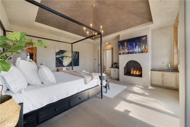 bedroom with a warm lit fireplace, an inviting chandelier, and a raised ceiling