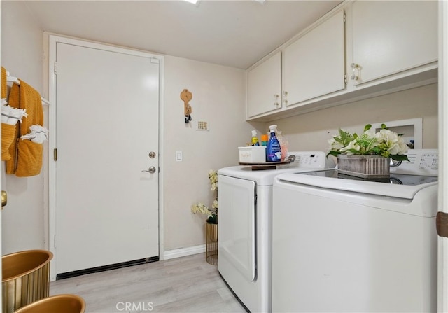 clothes washing area featuring light wood-style flooring, washing machine and clothes dryer, cabinet space, and baseboards