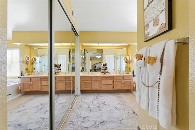 full bath featuring two vanities, a bath, marble finish floor, and a sink