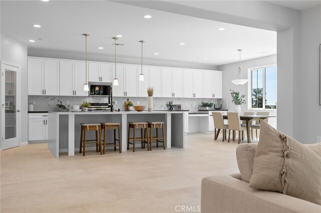 kitchen with a kitchen island with sink, recessed lighting, decorative backsplash, appliances with stainless steel finishes, and a breakfast bar area