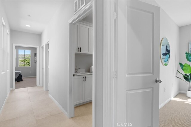 corridor featuring visible vents, baseboards, and light colored carpet