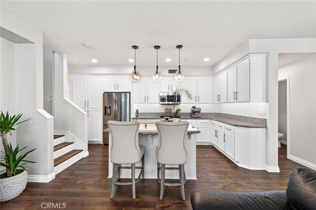 kitchen with an island with sink, stainless steel appliances, light stone countertops, and white cabinetry