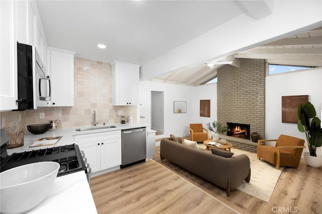 kitchen featuring a sink, appliances with stainless steel finishes, lofted ceiling with beams, open floor plan, and light wood finished floors