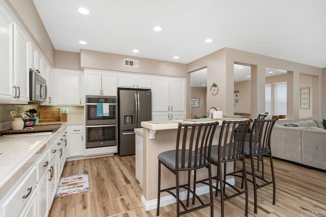 kitchen featuring white cabinets, stainless steel appliances, light wood-type flooring, a kitchen bar, and tile counters