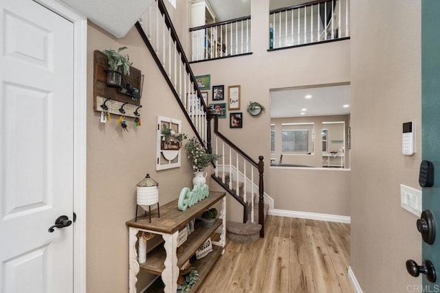 foyer entrance with a high ceiling, stairway, wood finished floors, and baseboards