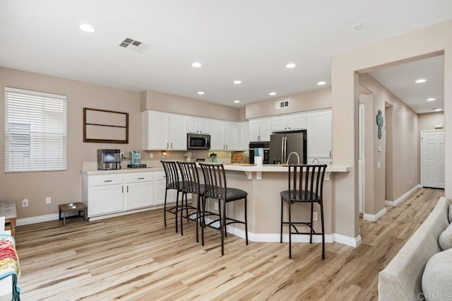 kitchen featuring a breakfast bar area, appliances with stainless steel finishes, light wood finished floors, white cabinetry, and visible vents