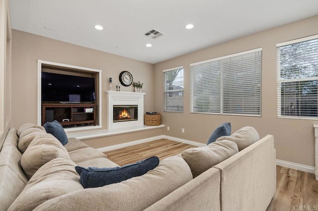 living room featuring baseboards, visible vents, light wood-style floors, and a glass covered fireplace