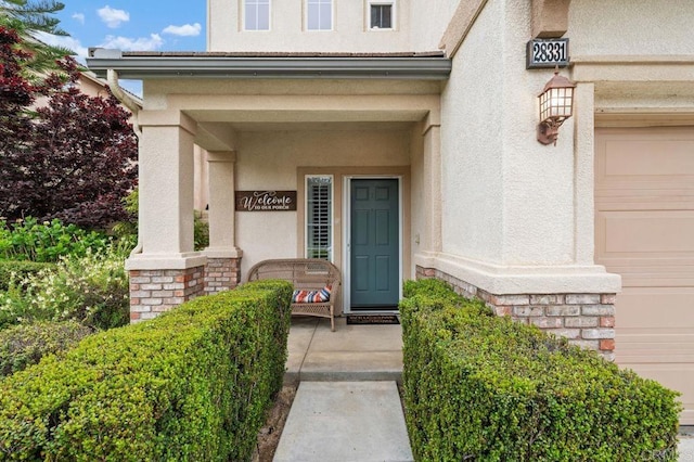 property entrance with stucco siding, stone siding, and covered porch