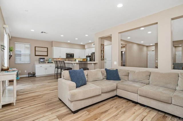 living area featuring baseboards, visible vents, light wood finished floors, and recessed lighting