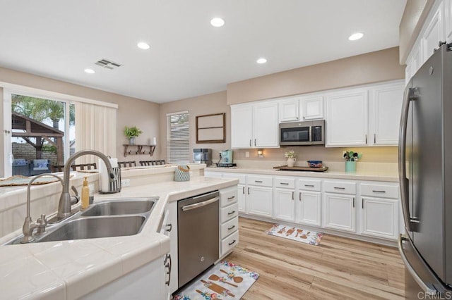 kitchen with tile counters, white cabinets, visible vents, a sink, and appliances with stainless steel finishes