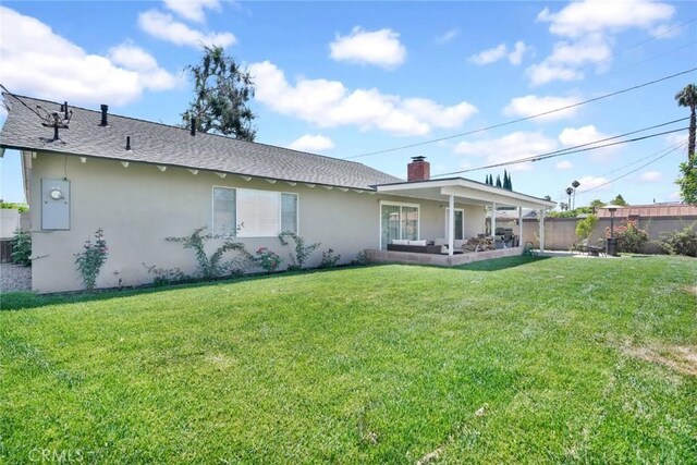 back of house with a chimney, fence, a shingled roof, a yard, and stucco siding