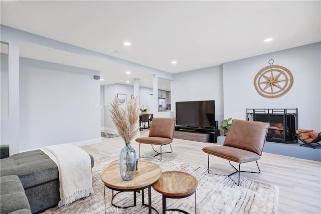 living room with recessed lighting, light wood-style floors, a fireplace with raised hearth, and baseboards