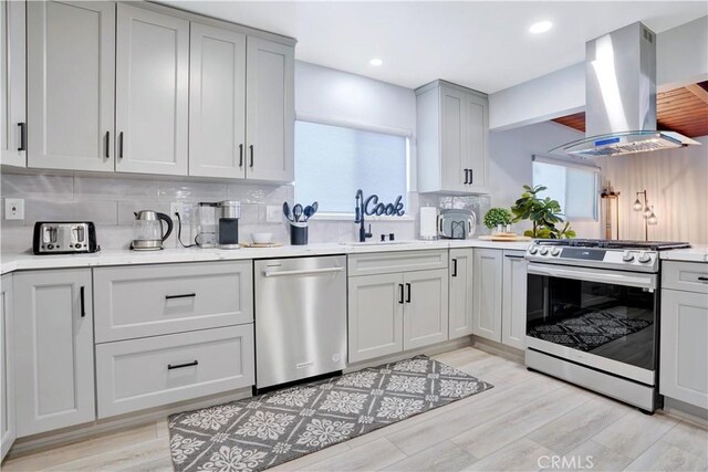 kitchen with stainless steel appliances, island exhaust hood, a sink, decorative backsplash, and light countertops