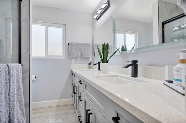 bathroom with baseboards, a sink, double vanity, and a stall shower