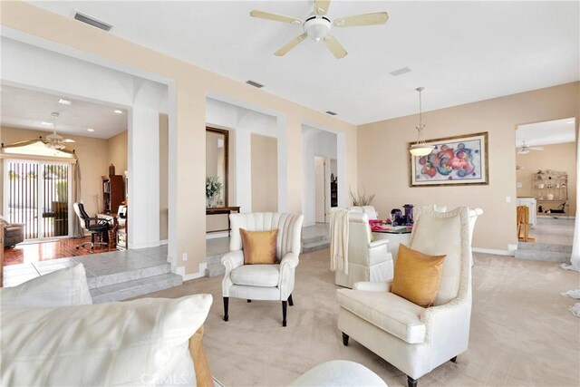 living area featuring baseboards, visible vents, light colored carpet, and ceiling fan
