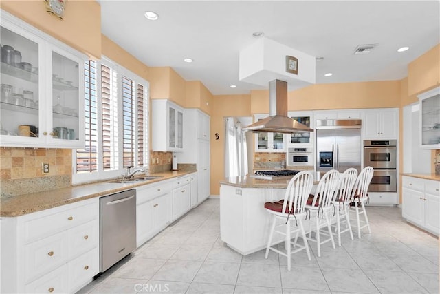 kitchen with stainless steel appliances, island exhaust hood, a sink, visible vents, and backsplash