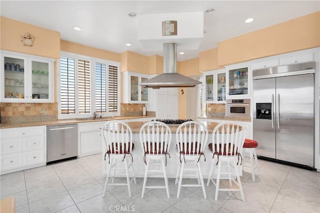 kitchen with island range hood, backsplash, appliances with stainless steel finishes, and a sink