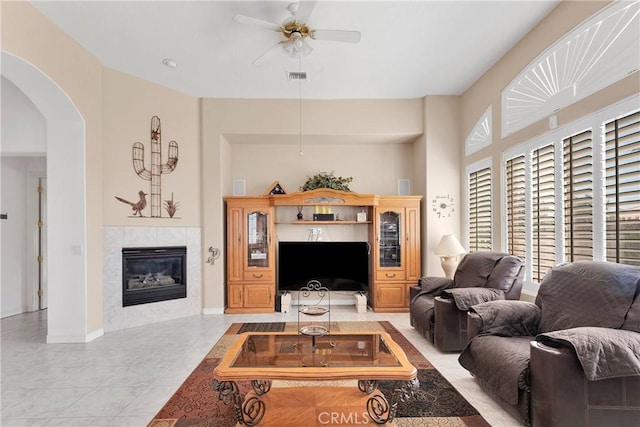 living area featuring a ceiling fan, arched walkways, a tiled fireplace, tile patterned flooring, and visible vents