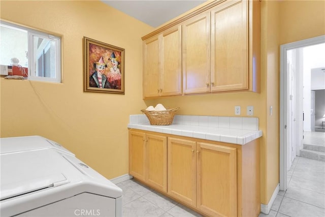 washroom with baseboards, cabinet space, washer and clothes dryer, and light tile patterned floors