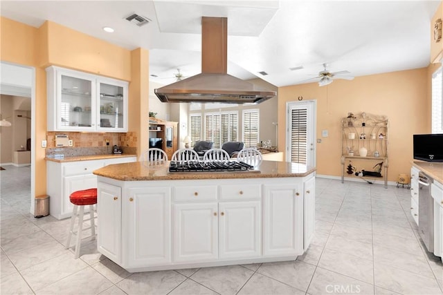 kitchen featuring island exhaust hood, backsplash, visible vents, glass insert cabinets, and ceiling fan