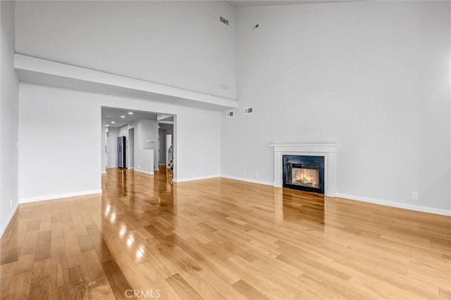 18324 Clark St Unit 315, Tarzana, CA 91356 - unfurnished living room with a glass covered fireplace, a high ceiling, light wood-type flooring, baseboards, and visible vents