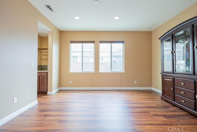 empty room with baseboards, a healthy amount of sunlight, wood finished floors, and visible vents